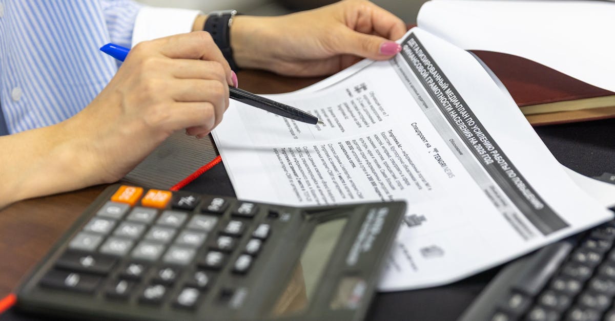Close-up of a person analyzing financial documents using a calculator and pen