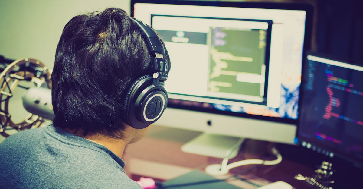 A programmer with headphones focuses on coding at a computer setup with dual monitors.